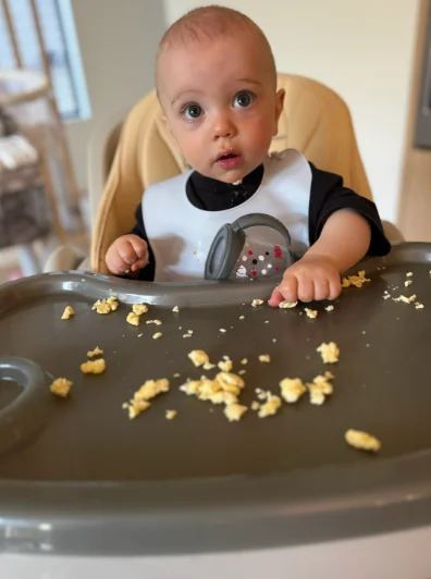 Auzzy in his high chair, mid-breakfast, scrambled eggs on the tray